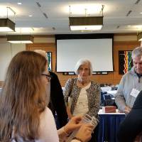 Older and younger people stand around a table